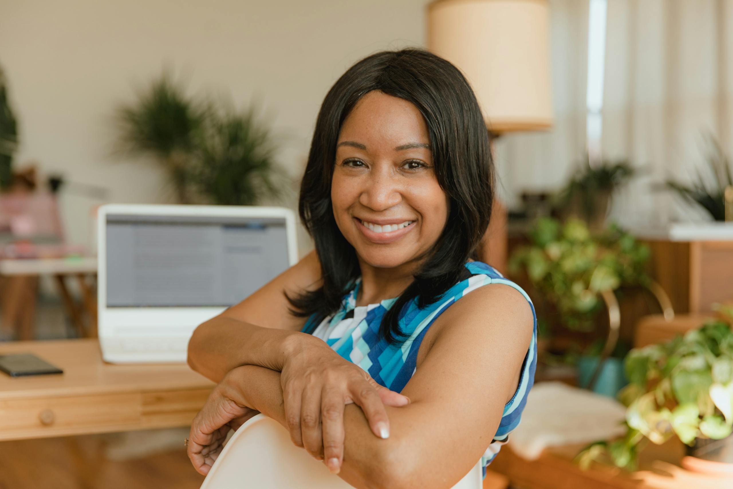 A smiling businesswoman sits confidently at her desk in a modern office setting.