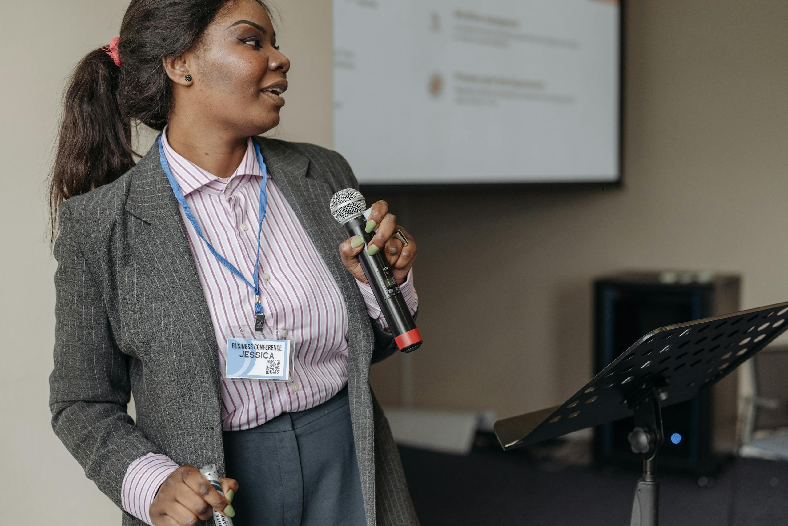 Woman in professional attire presenting at a business seminar with microphone.